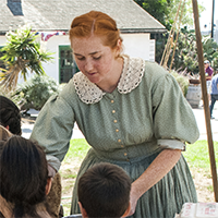 Volunteer in period accurate attire leading a group of children in an activity